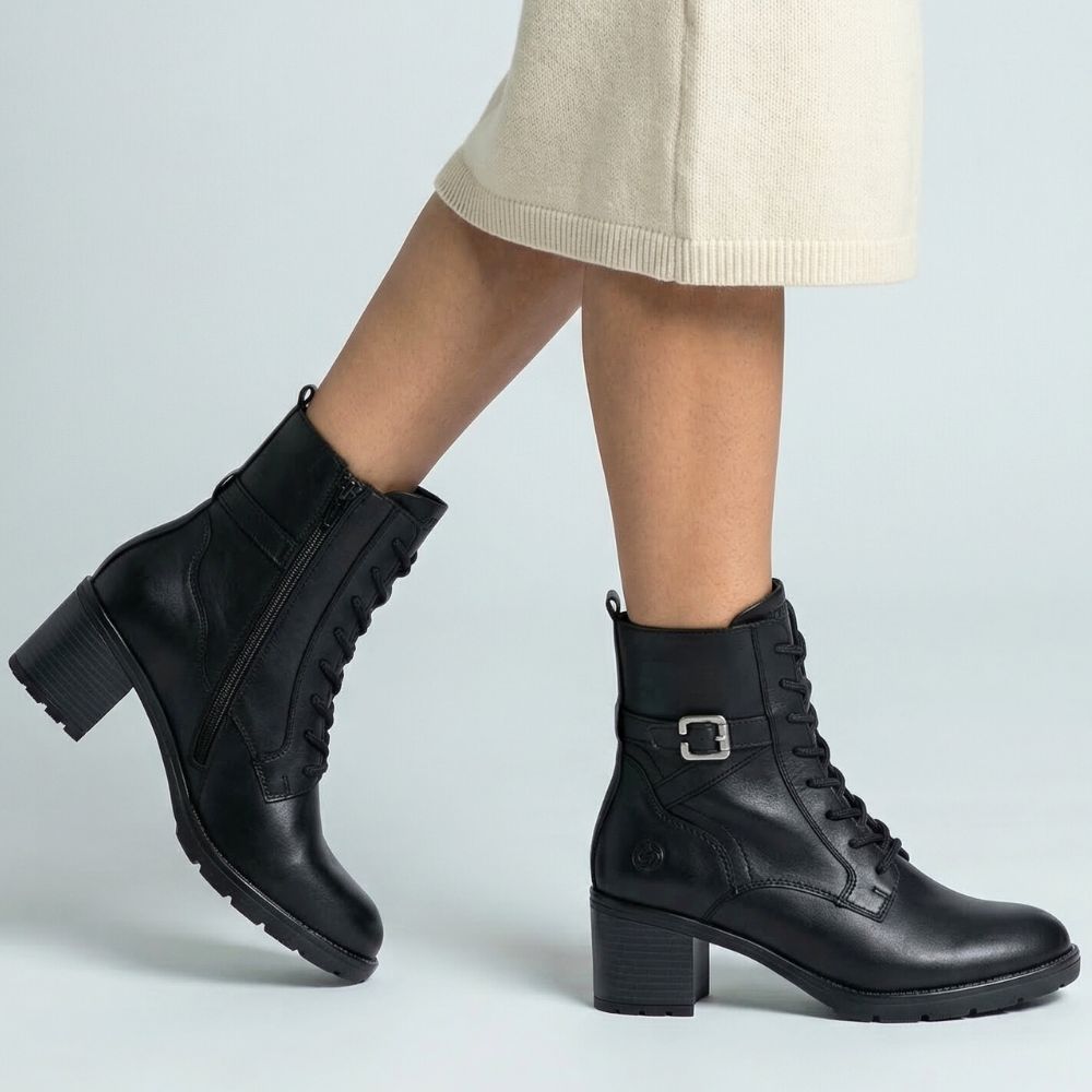 Black leather boots worn with a beige skirt on a light gray background