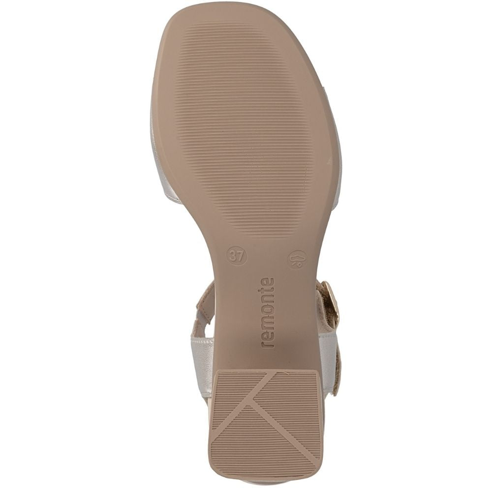 The outsole of a women's sandal shown from a top-down view, featuring a beige rubber sole with the brand name 'remonte' printed on it, alongside a metallic pale gold leather strap and a gold buckle.