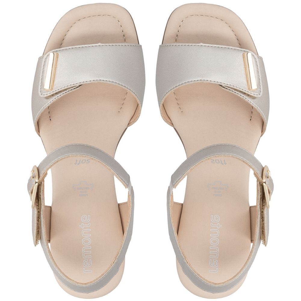 A pair of women's heeled sandals shown from a top-down view, featuring a metallic pale gold leather upper with a wide strap and a gold-tone buckle, set on a light beige footbed with an ankle strap and gold buckle.