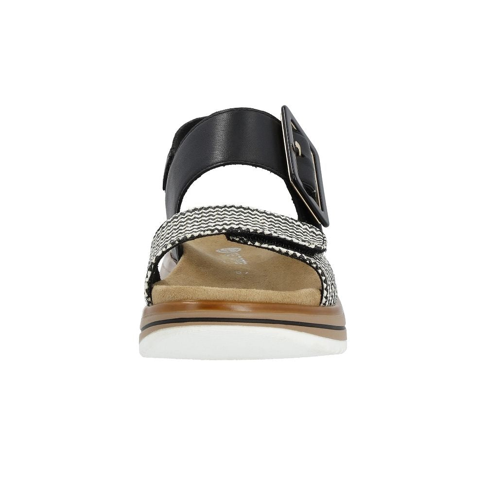 A single women's flat sandal shown from the front on a white background. The sandal features a black leather ankle strap with a square buckle, a black and white chevron patterned toe strap, a tan footbed, and a brown and white sole.