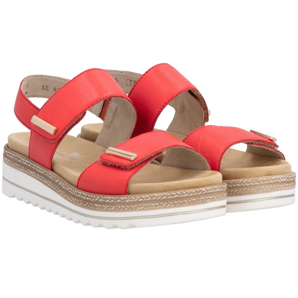 A pair of red leather platform sandals with two adjustable straps, gold-tone metal accents, and a white wavy outsole with jute-look trim detail, shown from a side profile on a white background.