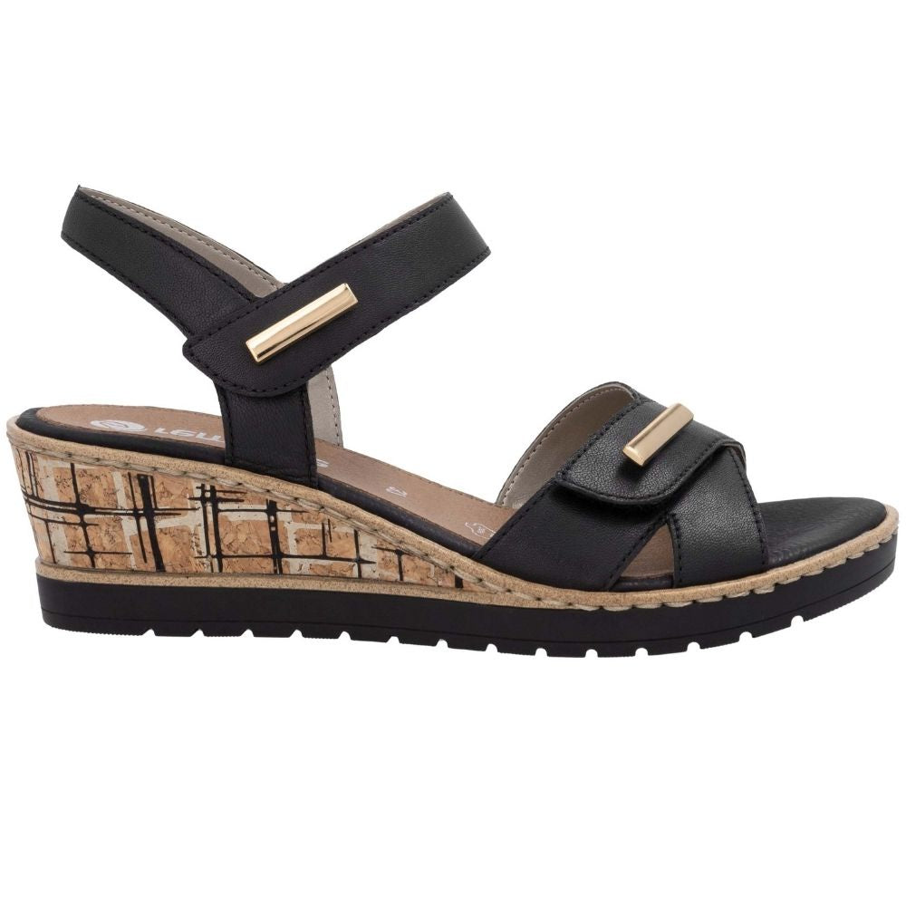 A black wedge sandal with a cork-textured wedge heel, black straps, and gold-tone metal accents, shown from a side profile view on a white background.