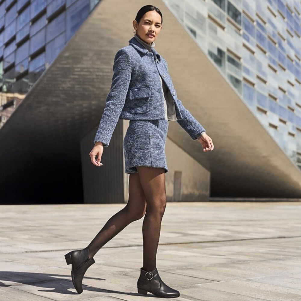 Woman in a blue textured suit walking on a wooden deck with modern architecture in the background