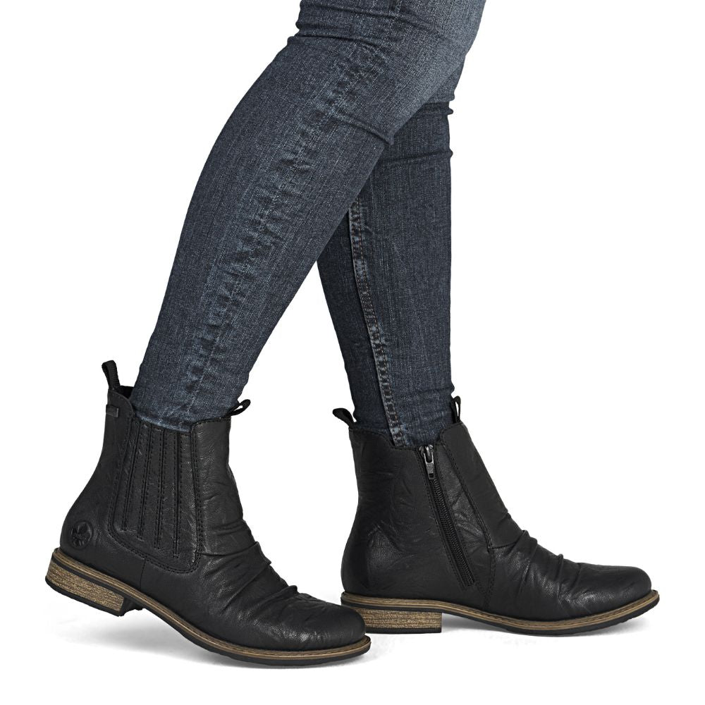 Black leather boots worn with blue jeans on a white background
