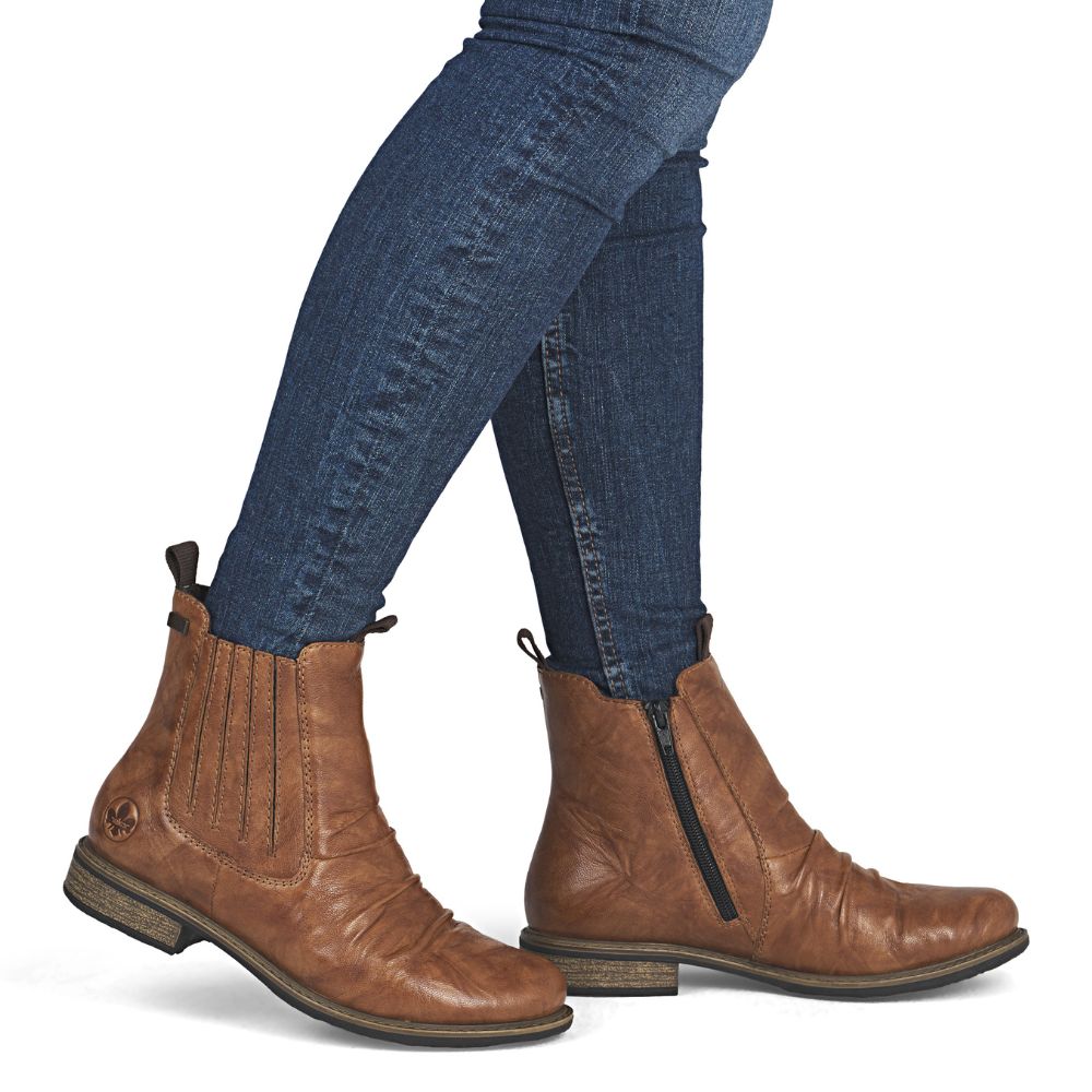 Brown leather boots worn with blue jeans on a white background