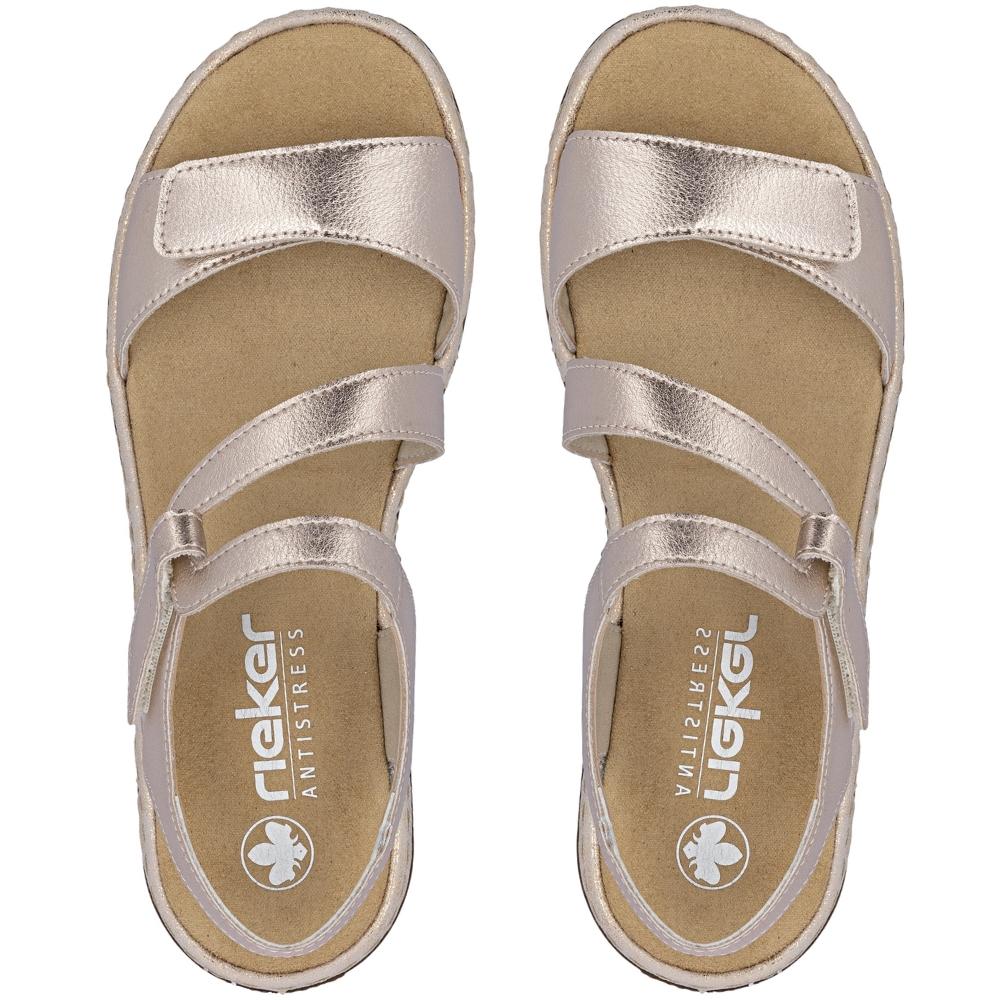 A pair of metallic rose gold slide sandals with adjustable straps and a tan insole, shown from a top-down view on a white background. The brand name 'Rieker' is visible on the footbed.