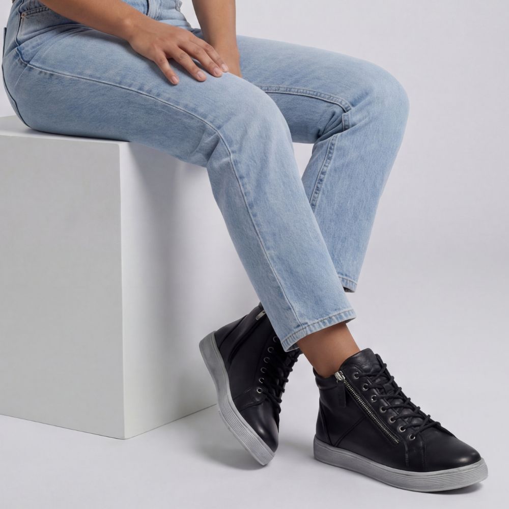 Person wearing black high-top sneaker boots with light gray soles, sitting on a white block.