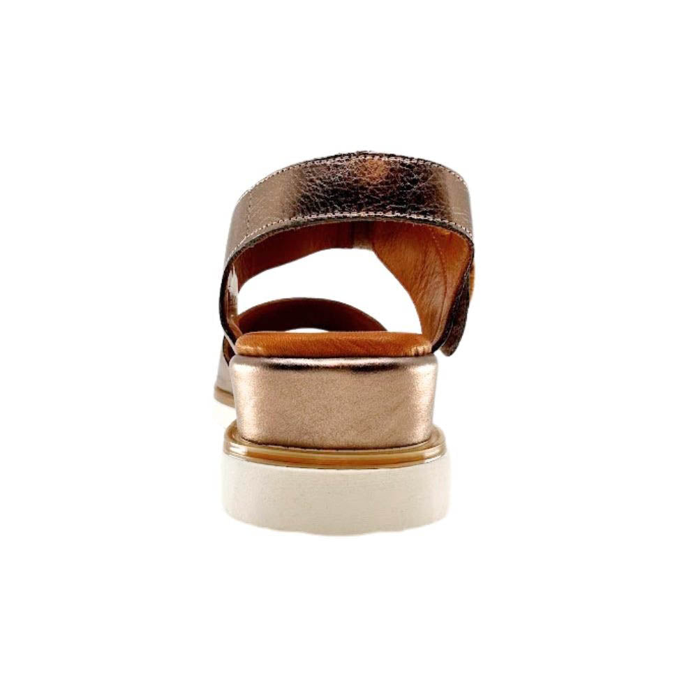 The back of a metallic bronze leather wedge sandal with a white sole, shown against a white background.
