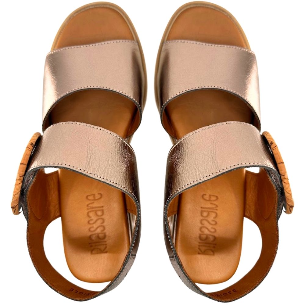 A pair of metallic bronze leather wedge sandals with a wooden circular buckle detail on the straps, shown in a top-down profile against a white background.