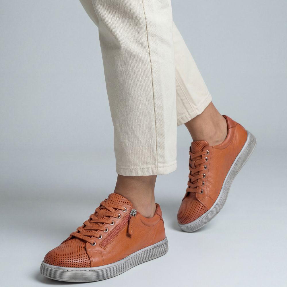 Orange sneakers worn with light-colored pants on a plain background