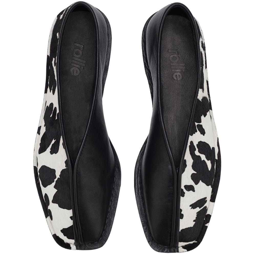 Pair of black and white cow print flats on a white background