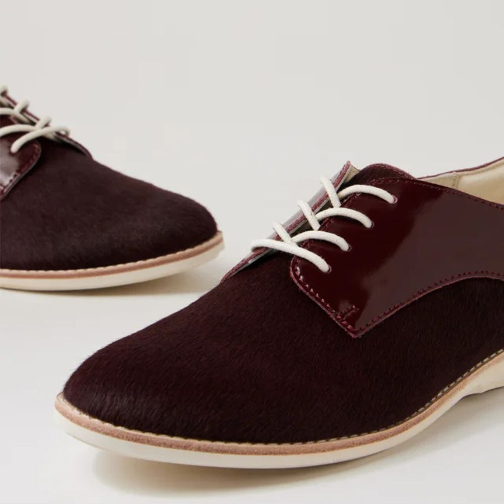 Pair of cherry burgundy leather shoes with white laces on a light background