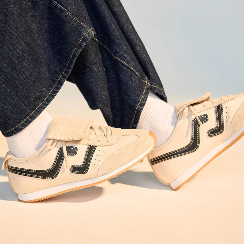 Person wearing dark blue jeans and cream sneakers with black accents in a studio background