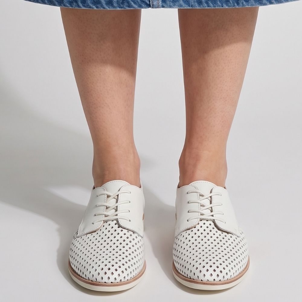White perforated leather lace-up shoes worn by a model, shown from the front against a clean white background.