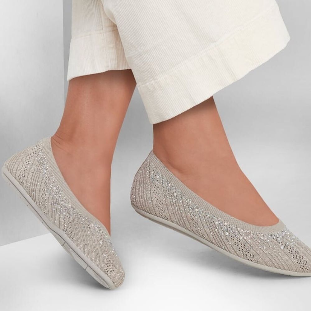 Taupe ballet flat shoes with sparkly embellishments worn with white pants on a light gray background