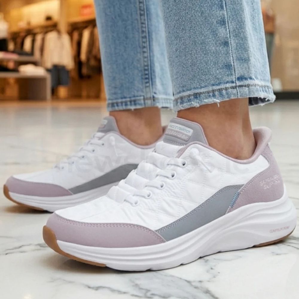 White low-top sneakers with light gray and dusty lavender panels, shown on a person wearing light-wash blue jeans in a retail store setting.