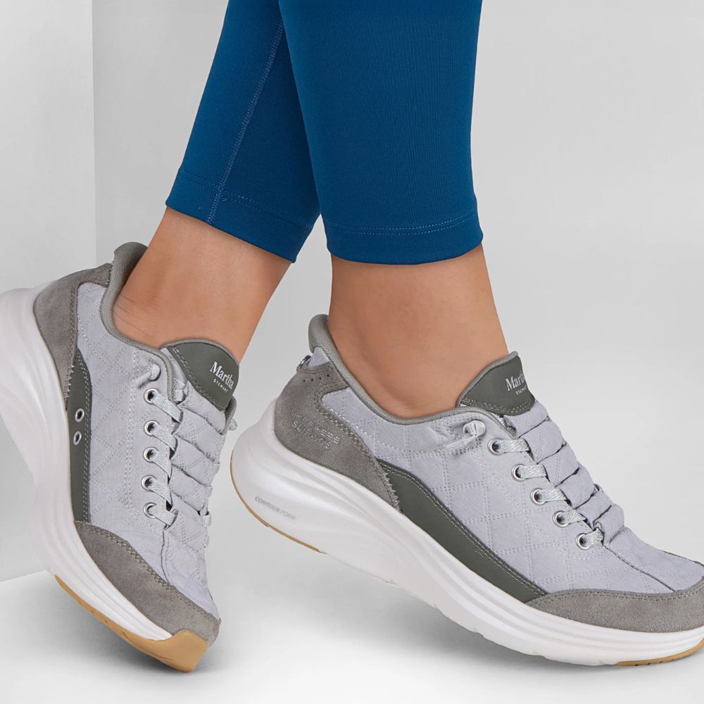 A pair of sage Slip-In sneakers worn with blue leggings, shown against a clean white studio background.