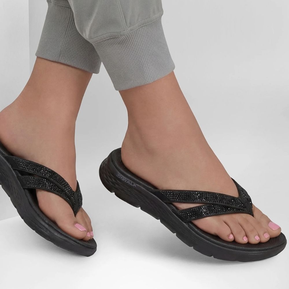 Black thong sandals with glittery straps worn by a model, shown from the side against a light gray background.