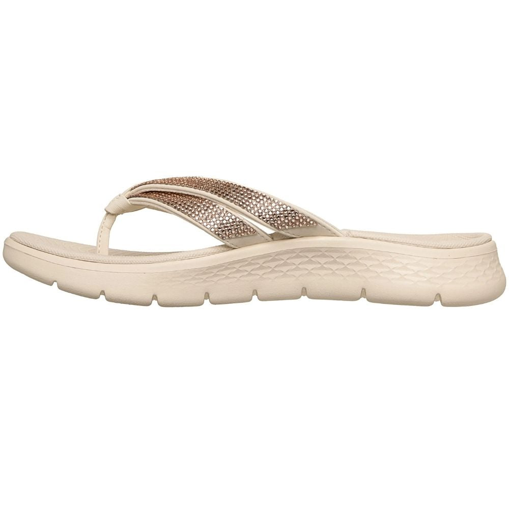 The inside view of a single beige flip-flop sandal with metallic rose gold rhinestone embellished straps, shown in a side profile on a white background. 