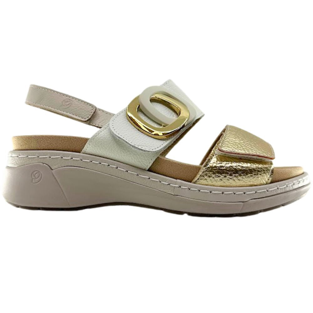 A women's platform wedge sandal with a light beige sole and heel strap, a cream leather strap with a large gold buckle, and a textured metallic gold toe strap.