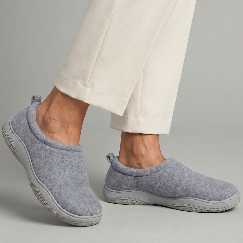 Person wearing grey slippers with cream pants on a grey background