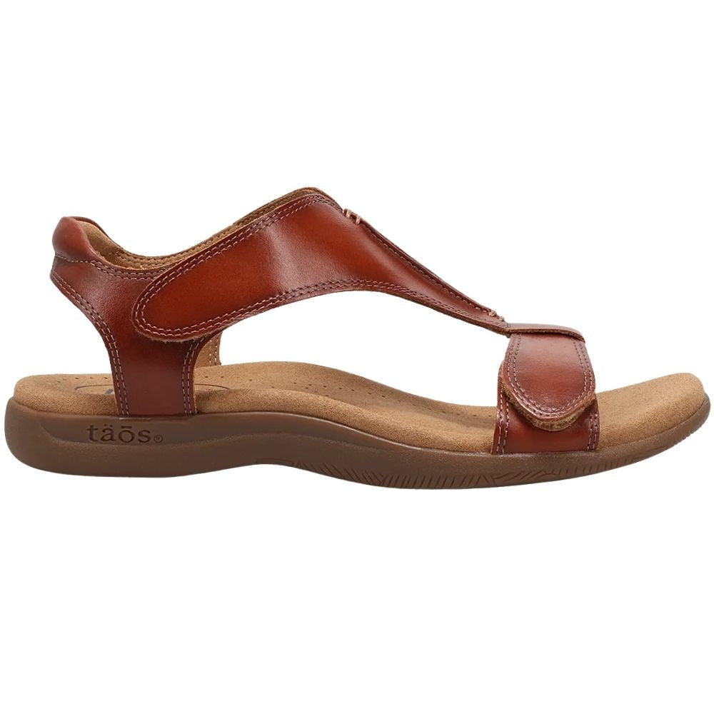 A Taos brand cognac leather T-strap sandal with a contoured brown sole, shown in a side profile view against a white background.