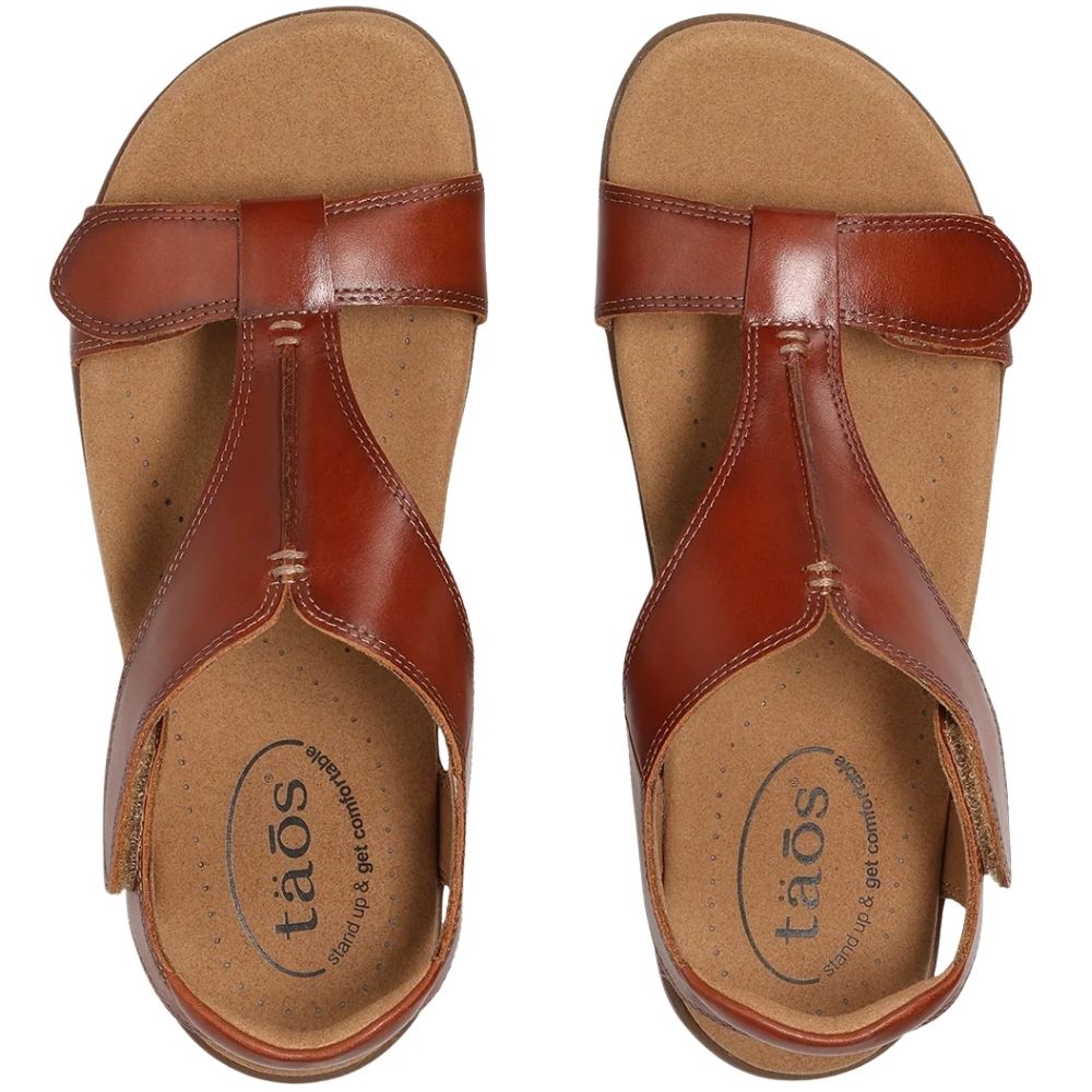 A pair of cognac leather T-strap sandals with brown straps, shown from a top-down view on a white background. The brand name 'taós' is printed on the footbed.