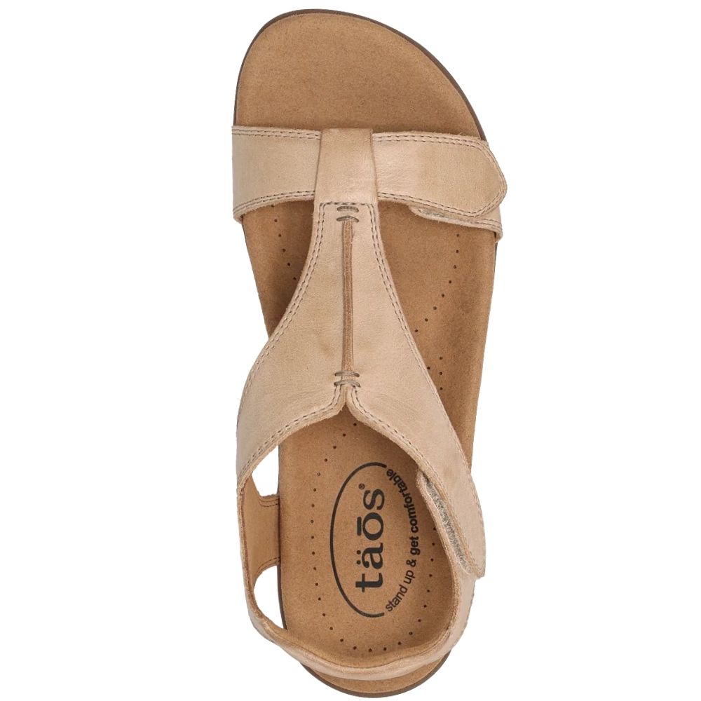 A single beige leather T-strap sandal shown from a top-down view on a white background, with the brand name 'taos' printed on the footbed.