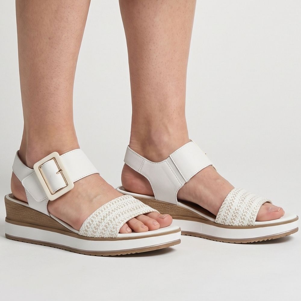 White platform sandals with woven front straps and a square buckle, shown on a model's feet against a light gray studio background.