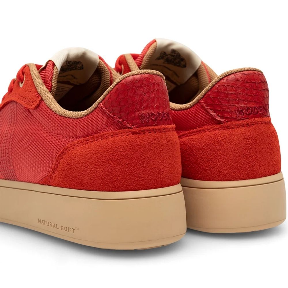 A pair of red low-top sneakers shown from the rear three-quarter angle, featuring textured red uppers, beige lining, and beige soles with 'NATURAL SOFT' printed on the side.