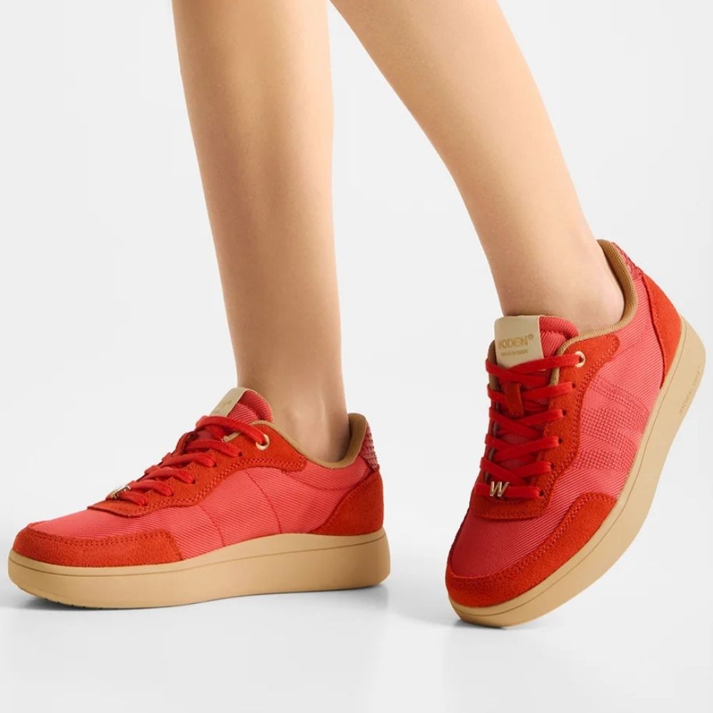 Red low-top sneakers with beige soles, shown on a model's feet against a light gray studio background.