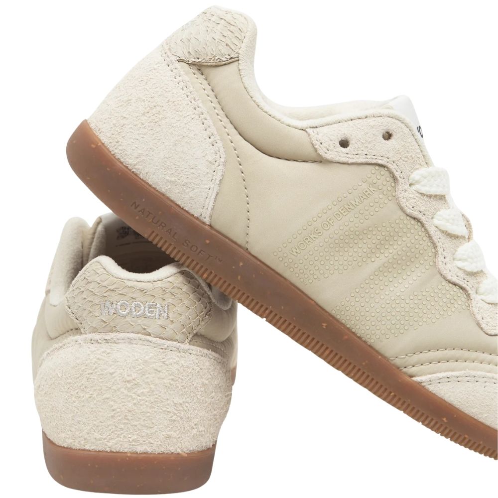 A pair of low-top sneakers in off-white recycled textile upper with brown gum soles, shown on a clean white background. One shoe is positioned upright showing the fish leather heel and side, while the other is angled diagonally showing the side profile and lace area.