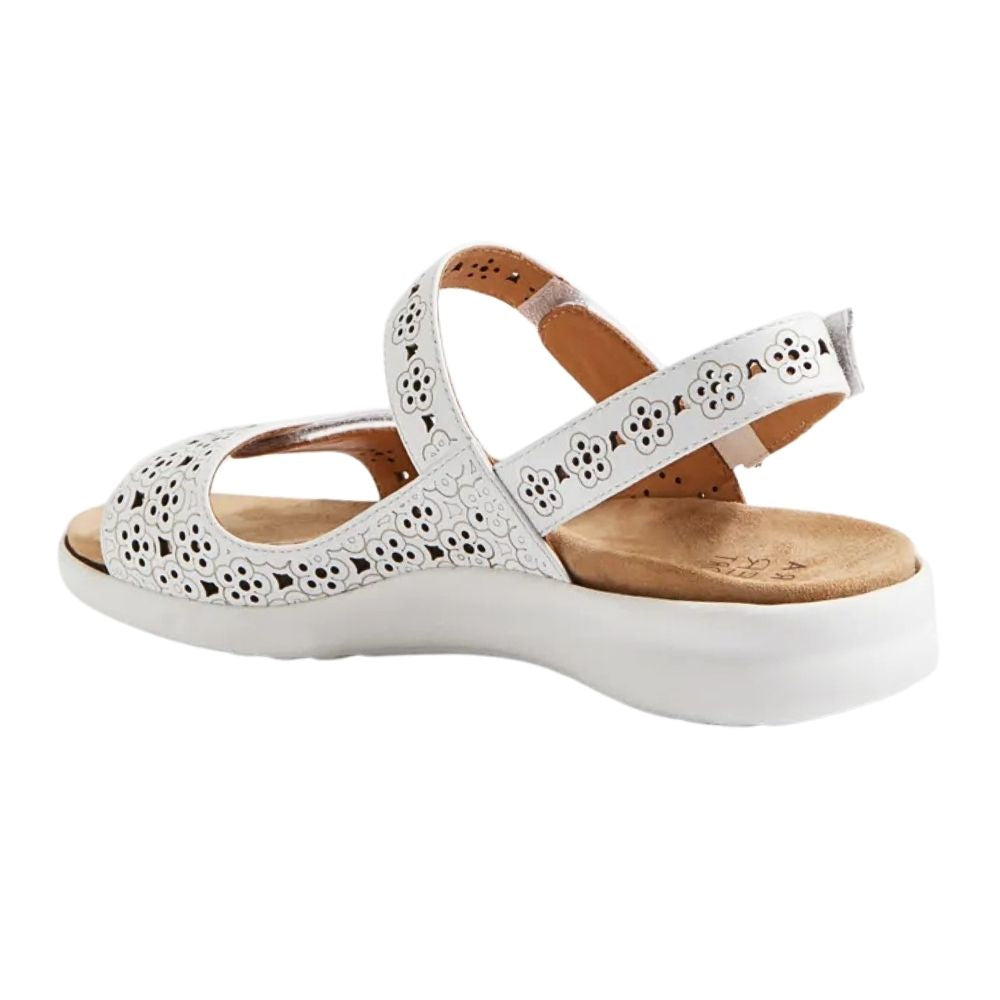 A white leather wedge sandal with floral cutout detailing on the straps, featuring a tan footbed and a thick white wedge sole.