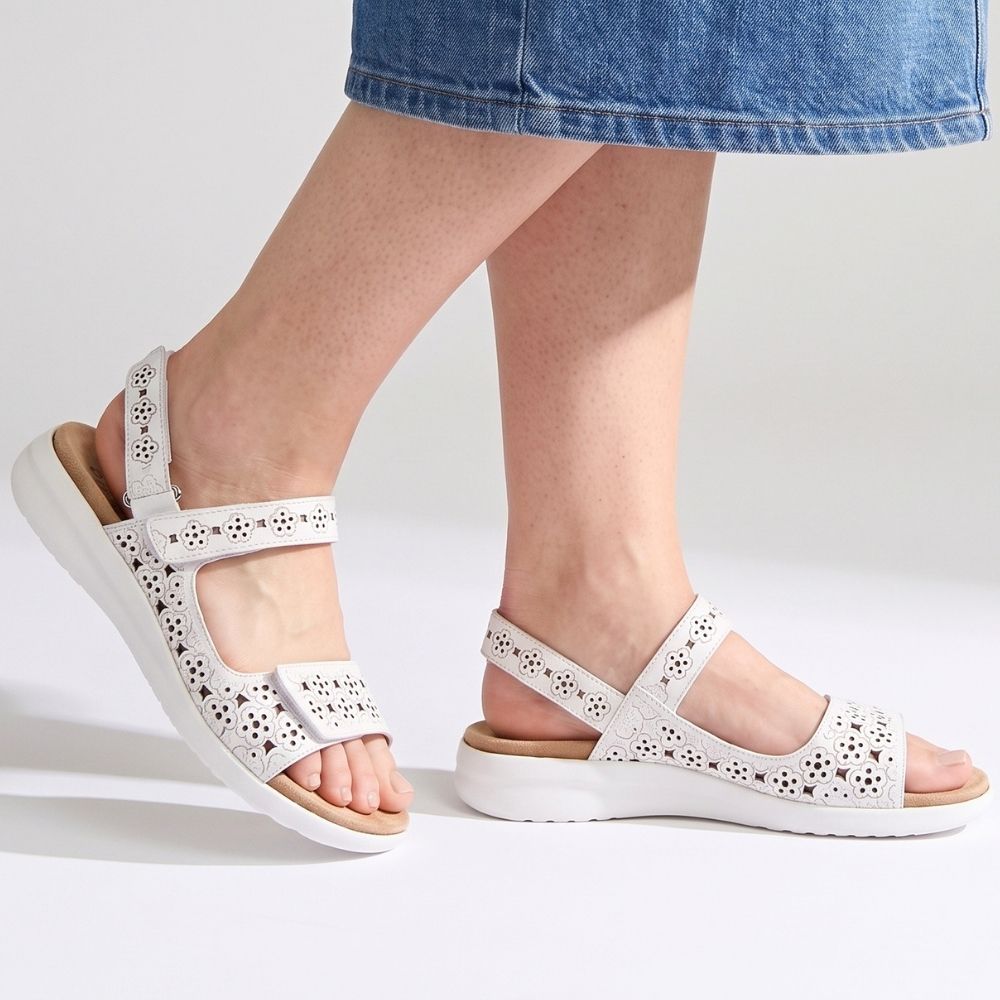White open-toe platform sandals with cutout straps and adjustable ankle straps, shown on a model's feet against a light gray studio background.