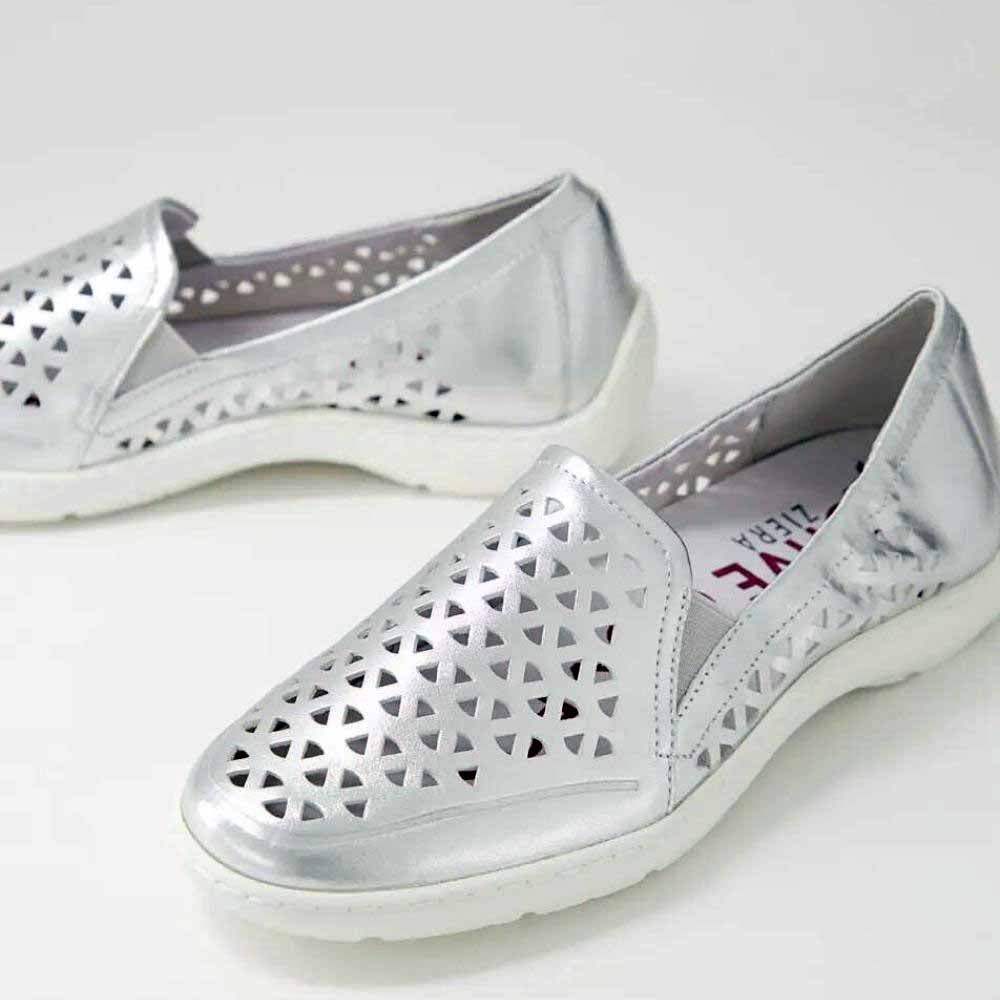 A pair of metallic silver slip-on shoes with geometric triangle cutouts on the toe and sides, featuring white soles, photographed on a light gray background.